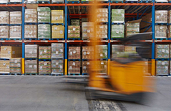 A photograph of a moving forklift in a warehouse in front of pallets of stock