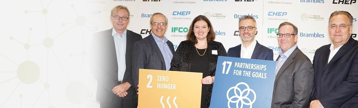 A banner image of a group photograph of business people holding a couple of cardboard SDG goals signs. The group is standing in front of a background banner of a collage of logos including the CHEP, IFCO, Brambles, and the Global Foodbanking Network logos,