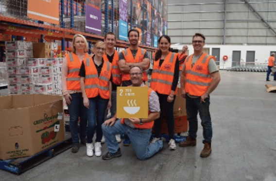 An image of a photograph a group of workers with fluorescent vests holding a 2nd SDG goal sign.