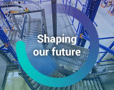 The words, 'Shaping our Future' inside a circle graphic overlayed on top of an image of a moving pallet on a conveyor belt