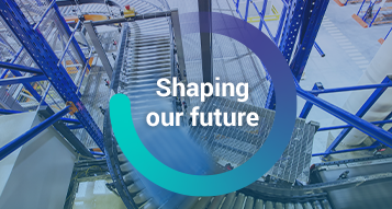 The words, 'Shaping our Future' inside a circle graphic overlayed on top of an image of a moving pallet on a conveyor belt