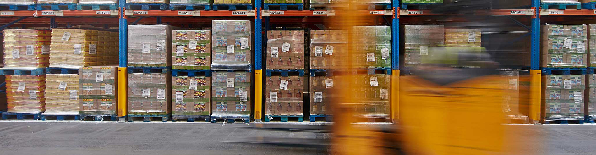 Supply Chain Solutions A photograph of a moving forklift in a warehouse in front of pallets of stock