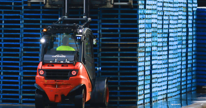 A photograph of a moving forklift in a warehouse in front of pallets of stock