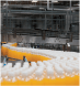 An image of hundreds of drinking bottles filled with orange liquid travelling on a conveyor belt in a warehouse environment